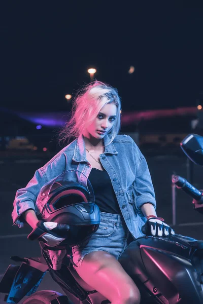 portrait of a girl in the rays of neon light on a motorbike at night in an empty parking lot