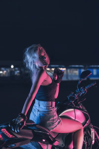在一个空旷的停车场 一个女孩在摩托车上的霓虹灯下的肖像 图库图片