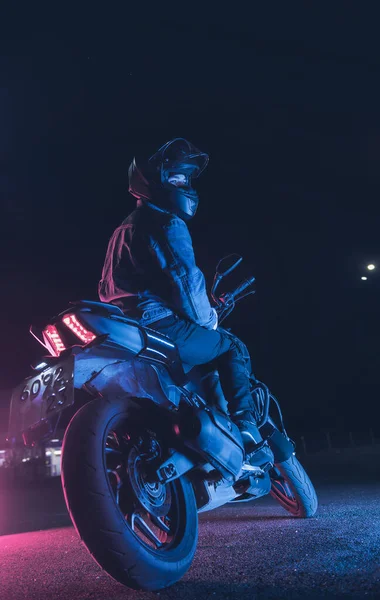 自転車愛好家は夜の駐車場でネオンライトのバイクに座っています — ストック写真
