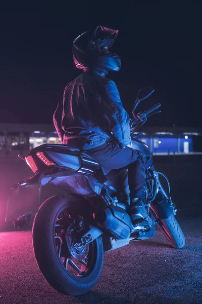 Motorradfahrer Sitzt Nachts Neonlicht Auf Leerem Parkplatz — Stockfoto