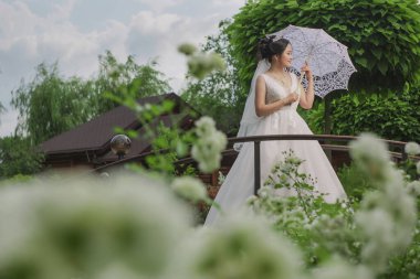 Doğanın arka planına karşı elinde açık şemsiyeyle poz veren Asyalı bir gelin.