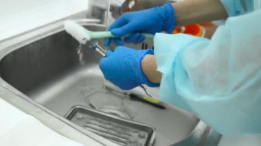 Temizlik, sterilizasyon ve diş hekimliğinde tıbbi aletleri dezenfekte etme. Diş hekimi asistanı dişçi aletlerini musluktan akan suyun altında fırçayla yıkıyor. Salgın sırasında yakın çekim koruma