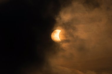 The Moon covering the Sun in a partial eclipse with dramatic cloud. clipart
