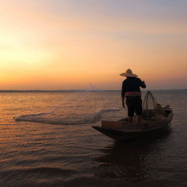 Asian fisherman with his wooden boat going to catching freshwater fish in nature river in the early during sunrise time