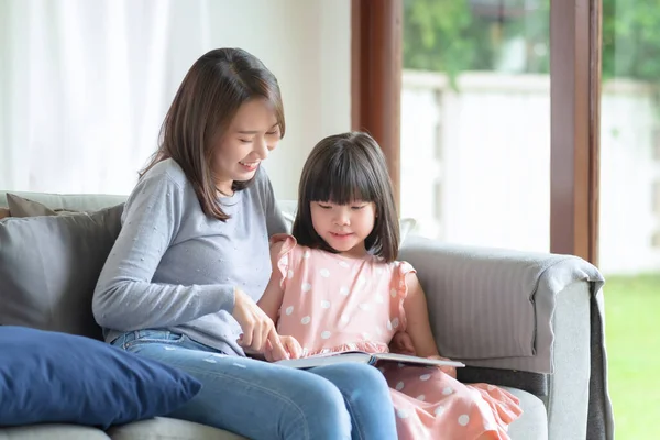 Happy asian mother teaching her cute kid daughter to studying in living room at home