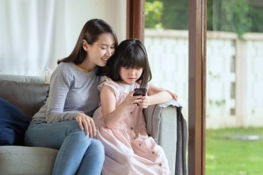 Asyalı anne ve kızı evdeki akıllı telefonla internet kullanmaktan zevk alıyorlar. 