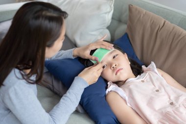 Asyalı anne, evde ateşi ve hastalığı olan çocuğuna bakıyor.