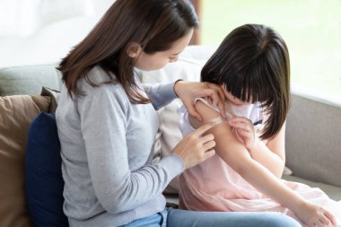 Asyalı anne evdeki kızına sargı bezi yapıştırıyor.