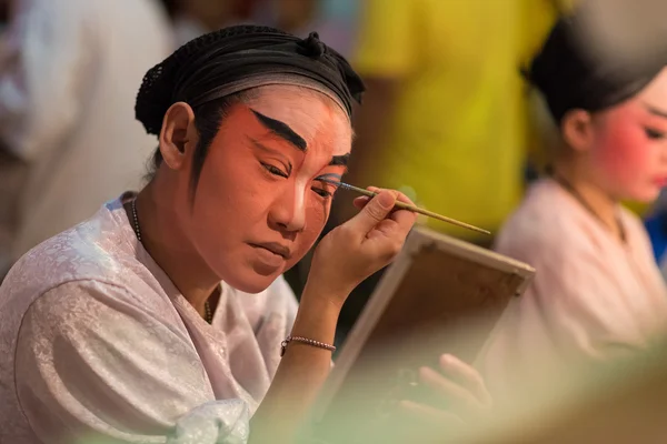 A Chinese opera actress painting mask on her face before the performance at backstage at major shrine in Bangkok's chinatown on October 16, 2015 in Bangkok,Thailand