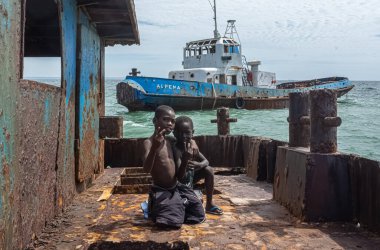Luanda / Angola - 11 / 10 / 2018: Eski paslı teknenin içindeki çocuklara bakın arka plandaki gemi ve denize, eski gemi mezarlığı deniz kıyısındaki