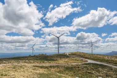 Rüzgâr türbinleri, yeşil ot tarlaları ve kirli yolları olan yüksek dağların manzarası...