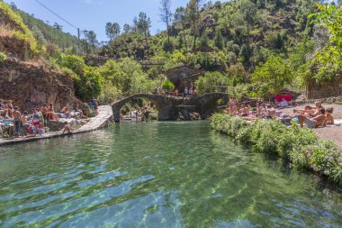 Piodao / Arganil / Portekiz - 08 22 22 2020: Portekiz 'in en tipik ve geleneksel köyü Piodao' daki doğal havuzların manzarası, insanların güneş banyosu, şist evler ve köprü kullanması