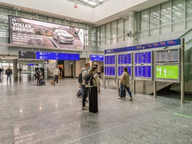 Frankfurt / Almanya 05 05 05 2021: Frankfurt havaalanı binasının iç manzarası, bavullar ve çantalarla yürüyen ve koridorda bilgi panosuna bakan insanlar