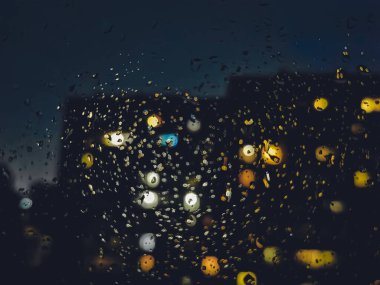 Pencerede yağmur damlaları, evden yansıyan ışık, bulanık arkaplan