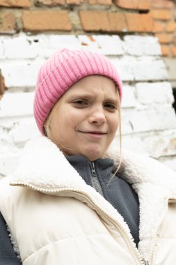 Belirsiz bir kız, neşeli bir şekilde kaşlarını çatıyor ve tuğla duvarın yanında sırıtıyor. İçten, samimi bir an, mizahı ve cesur kişiliğini yakalıyor.