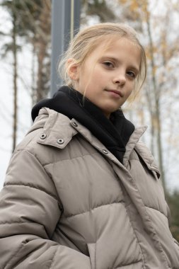 Kirli ceketli kızın yakın plan portresi sakin bakışları, yumuşak doğal ışık, orman arka planı, katmanlı kapüşonlu