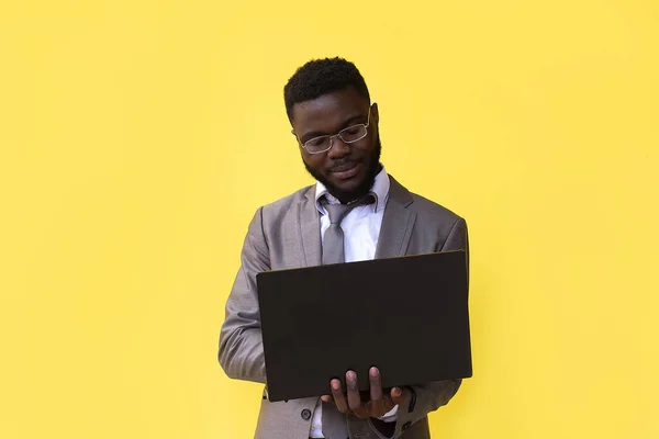 Mutlu, heyecanlı bir Afrikalı adamın görüntüsü. Laptop bilgisayarı kullanarak sarı arka planda izole edilmiş..
