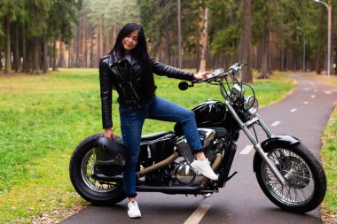 Güzel esmer, siyah deri ceketli motosikletli, elinde kaskla yazın parkta..