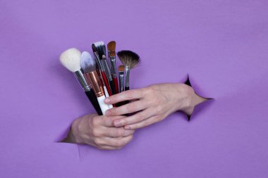 Ellerinizde profesyonel makyaj fırçaları, mor bir arka planda delikler. Metin için boşluk.