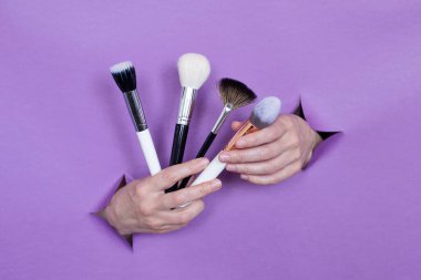 Ellerinizde profesyonel makyaj fırçaları, mor bir arka planda delikler. Metin için boşluk.