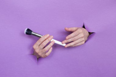 Ellerinizde profesyonel makyaj fırçaları, mor bir arka planda delikler. Metin için boşluk.