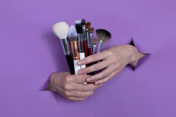 professional makeup brushes in your hands, on a purple background, holes in the background. Space for text.