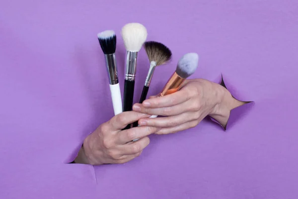 professional makeup brushes in your hands, on a purple background, holes in the background. Space for text.