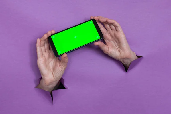 phone with green screen in hand on purple background, hand gesture, through the background hand slot.