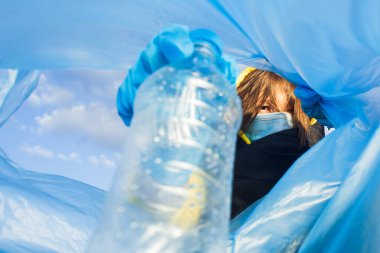 Bir kadın çöp kutusunun altına plastik bir şişe atar. Yakın plan, ekoloji ve dünyanın korunması kavramı..