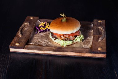 Lokantadaki ahşap tepside, karanlık bir arka planda çizburger..