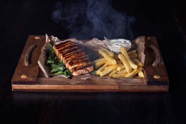 salmon fillet steak with french fries on a wooden tray, beautiful serving, dark background.