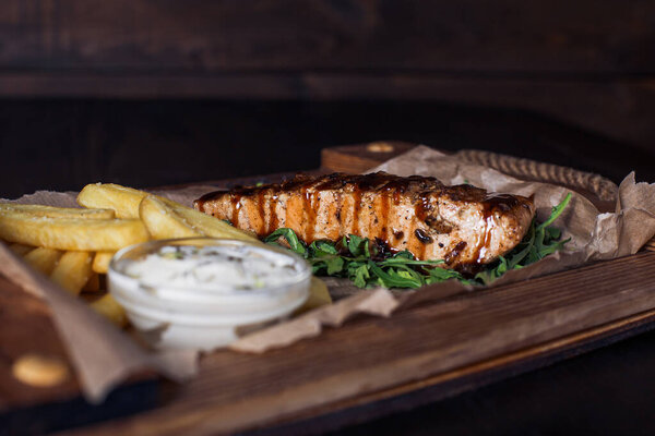 salmon fillet steak with french fries on a wooden tray, beautiful serving, dark background.