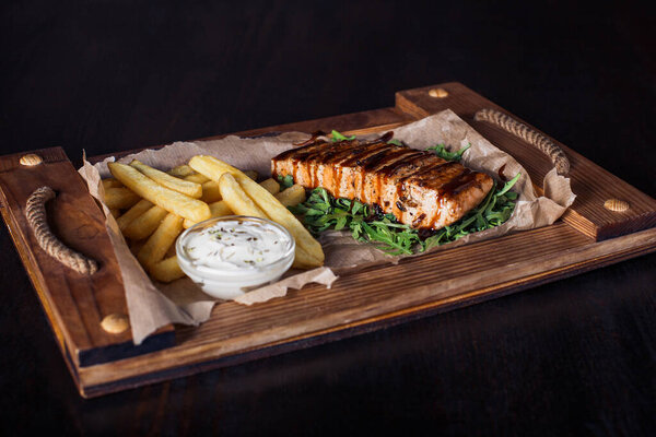 salmon fillet steak with french fries on a wooden tray, beautiful serving, dark background.