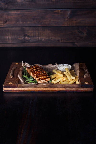 salmon fillet steak with french fries on a wooden tray, beautiful serving, dark background.