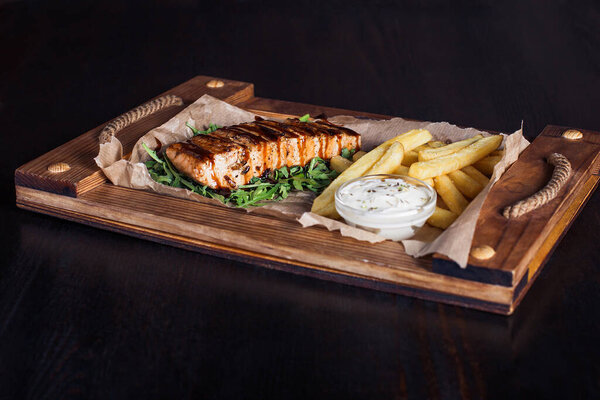 salmon fillet steak with french fries on a wooden tray, beautiful serving, dark background.