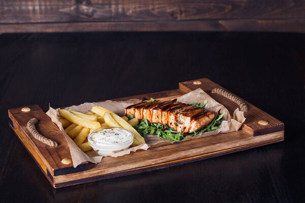 salmon fillet steak with french fries on a wooden tray, beautiful serving, dark background.