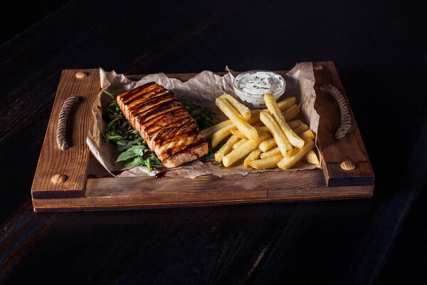 salmon fillet steak with french fries on a wooden tray, beautiful serving, dark background.