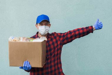 Erkek gönüllü koruyucu bir maske takıyor. Yanında bir kutu yiyecek ve hayır işi var..