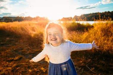 happy little girl runs through a field in nature, in the rays of the sunset.