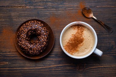 Kırsal ahşap arka planda, kapuçino ve çikolata kaplı çöreklerle lezzetli bir kahvaltı.