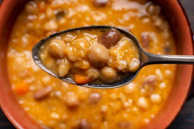 Önplanda, yukarıdan bakıldığında, leziz bir organik ve vejetaryen çorbası, baklagiller, sebzeler ve mısır gevrekleri hazır.