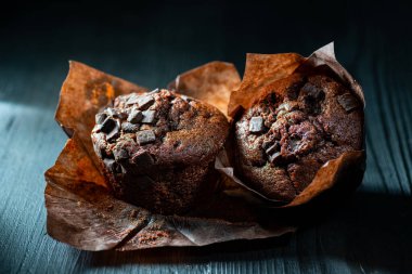 Koyu ahşap bir arka planda, yan otlatma ışığı, ön planda siyah çikolata parçalarıyla çörekler. Durgun hayat