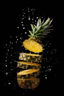 Taze ve dilimlenmiş ananas ve siyah arka planda meyve suyu sıçraması.