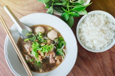 Beyaz kasede domuz etli şehriye çorbası ve pilav buğulama, ahşap masada fesleğen yaprağı. Tayland usulü. Üst Manzara. Düz yatıyordu. Erişteli çorba kasesine odaklan..
