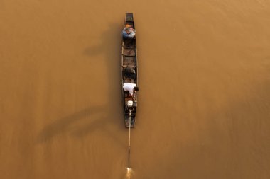 Asyalı bir balıkçı güneş doğarken bir nehre balık ağı atarken geleneksel ahşap balıkçı teknesinde duruyor. Tayland 'da kırsal bir yer. Balıkçıya odaklan..