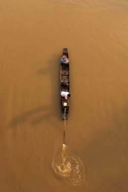 Asyalı bir balıkçı güneş doğarken bir nehre balık ağı atarken geleneksel ahşap balıkçı teknesinde duruyor. Tayland 'da kırsal bir yer. Balıkçıya odaklan..