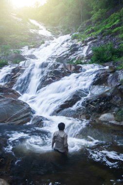 Gün doğumunda derin bir tropikal yağmur ormanında saf şelaleye bakan bir adam. Mae Wong Ulusal Parkı, Tayland. Keşif, eğlence, eğlence, seyahat kavramları. Uzun pozlama.