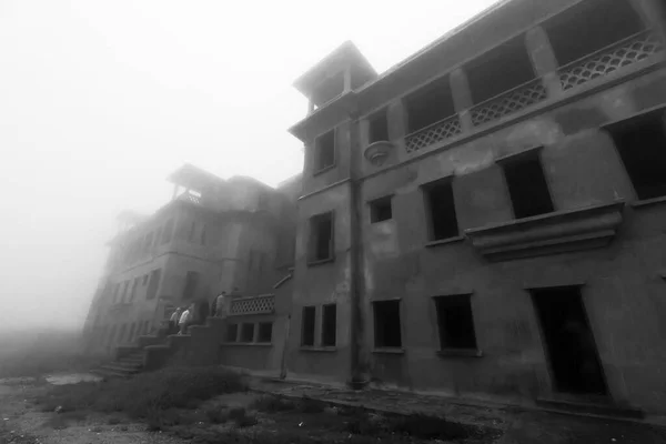 霧の中で放棄されたボコールパレスホテルの暗い神秘的な雰囲気 観光客のグループはボコールカジノホテルへのメインの入り口を歩く カンボジアのカンポット ボルコール山 モノクローム ソフトフォーカス — ストック写真