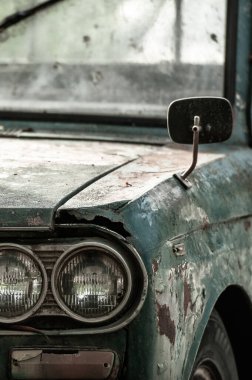 Caddeye park edilmiş eski bir zeytin yeşili arabanın ön tarafı. Antika araba, klasik yan ayna, far, boya kabuğu, eski yeşil renkler, pürüzlü erozyon metal ütü. Farlara odaklan..