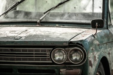 Caddeye park edilmiş eski bir zeytin yeşili arabanın ön tarafı. Antika araba, klasik yan ayna, far, boya kabuğu, eski yeşil renkler, pürüzlü erozyon metal ütü. Farlara odaklan..